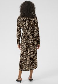 Abito midi con stampa leopardata in tonalità tan e nero, caratterizzato da maniche lunghe, una vita cintata e una texture liscia. Abbinato a sandali con tacco.