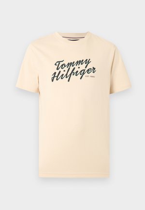 Beež lühikeste varrukatega t-särk, mille rinnal on mustas kursiivkirjas trükitud tekst "Tommy Hilfiger EST. 1985", ümara kaelusega.
