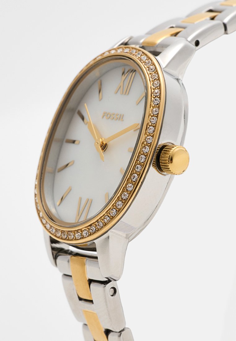 Montre Fossil en argent et ton or avec un boîtier rond, un cadran blanc, des chiffres romains, une lunette ornée de cristaux et un bracelet en métal.