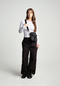 Svarta lösa byxor med matt yta, i kombination med en vit långärmad topp. En liten svart crossbody-väska bärs på vänster axel.