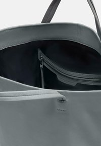 Graue Leder-Shopper-Tasche mit glatter Oberfläche, ausgestattet mit einer Reißverschlusstasche innen und einem weichen Innenfutter. Taperte Kanten und stabile Griffe.