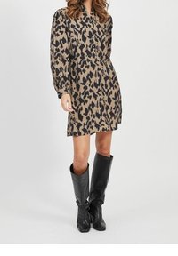 Vestido de estampado animal en tela marrón y negra con botones en la parte delantera, mangas largas y un corte holgado. Combinado con botas negras hasta la rodilla.