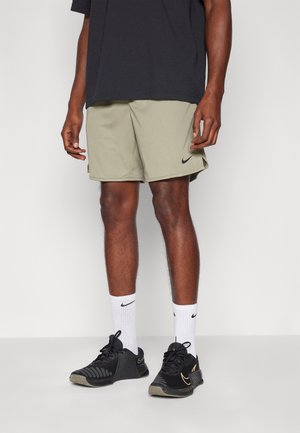 Olive green athletic shorts with a black Nike logo, paired with black and gold Nike shoes and white Nike socks, worn by a person standing.