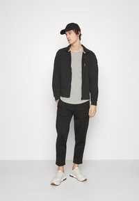 Juodas užtrauktukas striukė ant pilkos marškinėlių, derinama su juodom jogger kelnėm ir baltais sportbačiais. Kepurė taip pat juoda, užbaigianti aprangą.