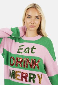Maglione a righe rosa e verde con testo decorativo in paillettes. Il testo recita "Eat DRINK MERRY" in paillettes multicolori.