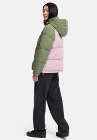 Gevoerde jas met een groen en roze kleurblokontwerp, een capuchon en een ritssluiting. Gekocht met losvallende zwarte jeans en zwarte schoenen.