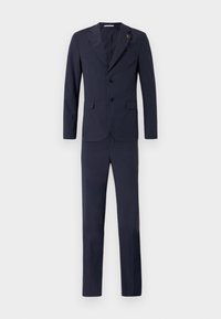 Kék öltöny, amely egyszerű zakót tartalmaz, két fekete gombbal, valamint kifordult hajtókával és illeszkedő nadrággal. Sima textúra és testreszabott illeszkedés.