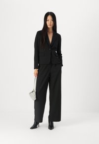 Blazer nero su misura con un solo bottone, abbinato a pantaloni neri a gamba larga. Accessoriato con una borsa scintillante argento e tacchi neri.