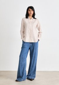 Striped button-up shirt in beige and white, paired with loose blue denim jeans. Smooth fabric with classic collar and buttons.