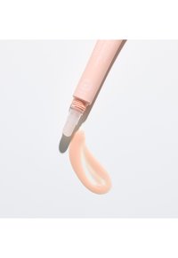 Un tubo di balsamo labbra dal delicato colore rosa con un applicatore trasparente, che distribuisce una striscia liscia e curvata di balsamo su uno sfondo bianco.