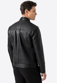 Schwarze Lederjacke mit einem taillierten Design, glatter Textur und Stehkragen. Sie verfügt über genähte Nähte und einen Bund mit einem leichten Glanz.