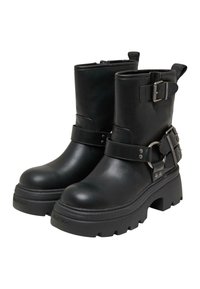Botas de piel negra hasta el tobillo con suela gruesa, con correas y acentos de hebilla de metal. Textura suave y diseño de punta redondeada.