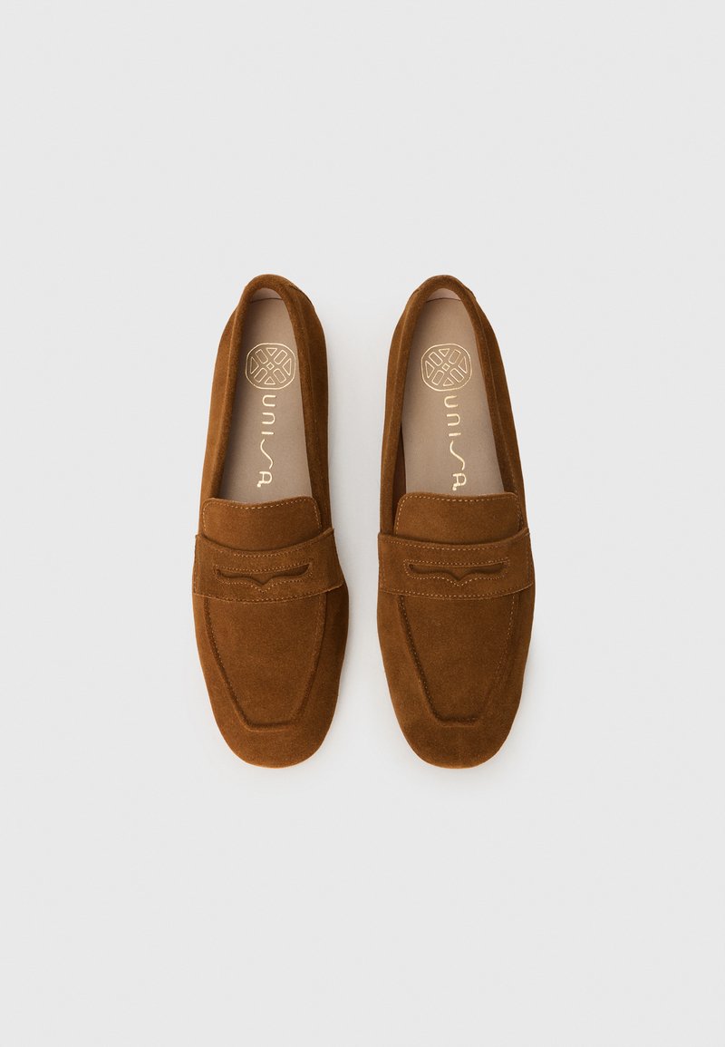 Mocassins en cuir suédé marron avec une texture lisse, dotés d'un bout arrondi et d'un détail de couture décoratif sur le coup de pied. Semelles plates.
