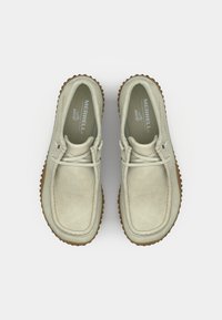 Zapatos de ante de color claro con punta redondeada, detalles de costura y suela de goma marrón texturizada. Cintas ajustables para un mejor ajuste.