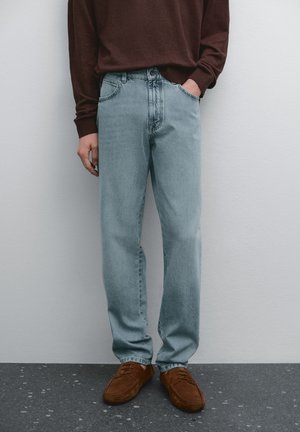 Light blue denim jeans with a straight fit, featuring a five-pocket design and faded texture. Paired with a brown long-sleeve shirt.