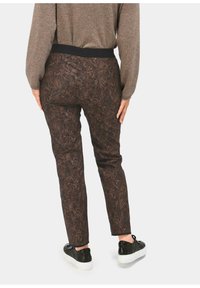 Bruine, gemusterde broek met een zwarte elastische tailleband, aansluitend ontwerp en textuur met bloemenpatroon; gecombineerd met zwarte sneakers.
