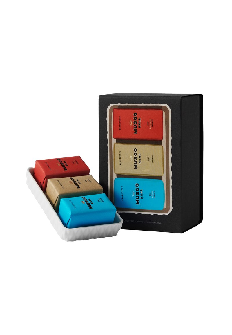 Geschenkset mit drei Seifen, verpackt in rotem, beigem und blauen Papier, präsentiert in einer weißen, gewellten Schale, mit einer schwarzen Verpackungsbox.