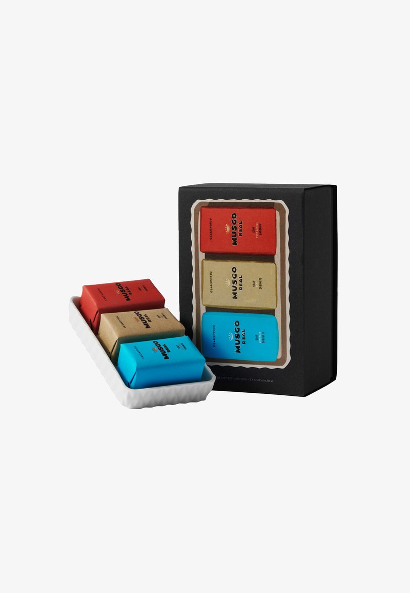 Gift set featuring three bars of soap wrapped in red, beige, and blue paper, displayed in a white scalloped dish, with a black box packaging.