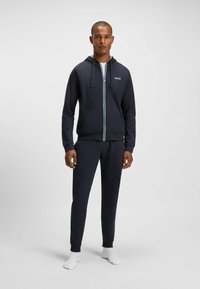Marine hoodie en jogger set gemaakt van zachte stof, met een frontale rits, twee zakken en een logo-accent op de borst. Gladde textuur.
