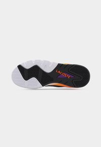 Semelle d'une chaussure Lacoste en noir, blanc et orange avec une bande de roulement texturée et le logo "LACOSTE" en orange sur un fond noir et violet.