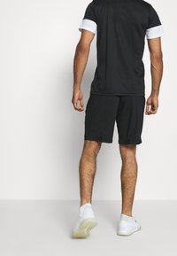 Musta urheiluasu, johon kuuluu lyhythihainen paita ja polvipituinen shortsit. Paidassa on valkoiset hihansuut, ja se on valmistettu kevyestä kankaasta, yhdistettynä valkoisiin lenkkareihin.