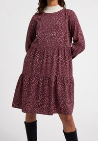 Robe à motifs rouges avec un design en plusieurs niveaux, manches longues et un col texturé blanc. Présente un motif floral dans des nuances de bleu et de crème.