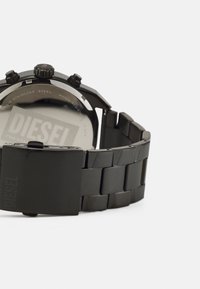 Schwarze Edelstahl-Uhr mit strukturiertem Armband, rundem Gehäuse, Chronographen-Tasten und einer Schließe, die das "DIESEL"-Logo zeigt.