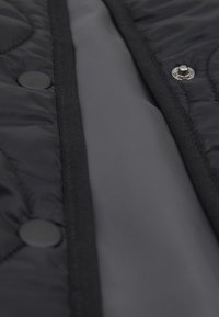 Gros plan d’un tissu matelassé noir avec un bouton pression et une partie d’une doublure intérieure lisse visible.