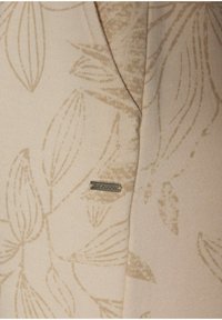 Beige Oberteil mit tonal floralem Muster, strukturiertem Stoff und silbernem Logo-Detail. Mit V-Ausschnitt und abgerundetem Saum.