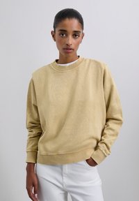 Langärmeliges Sweatshirt mit Rundhalsausschnitt aus weichem, hellgelbem Stoff mit strukturierter Oberfläche und gerippten Bündchen, kombiniert mit weißen Hosen.