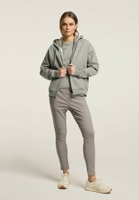 Szara bluza z kapturem zapinana na zamek, noszona na dopasowanej bluzce z długim rękawem, w zestawieniu z jasnoszarymi, slim-fit spodniami i białymi trampkami. Tkanina z fakturą na całej powierzchni.