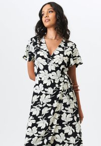 Wrap dress in black fabric featuring a white floral pattern. Short sleeves, V-neckline, and tie detail at the waist. Smooth texture.