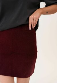 Burgundská pletená sukně s žebrovaným pasem, hladkou texturou a přímým střihem. Tkanina vypadá měkce a je mírně elastická.