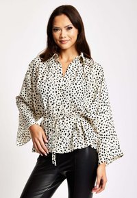 White blouse with black speckles, long bell sleeves, and a tied waist. Paired with black, form-fitting pants. Smooth fabric texture.