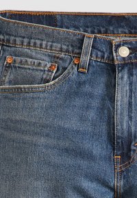 Blauwe denim jeans met een klassieke vijf-pocket ontwerp, contrasterende oranje stiksels, metalen knoopsluiting en een soepele textuur.