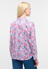 Camicia a maniche lunghe floreale con stampa rosa, blu e bianca. Design con colletto, orlo curvo e maniche con polsini. Tessuto leggero.