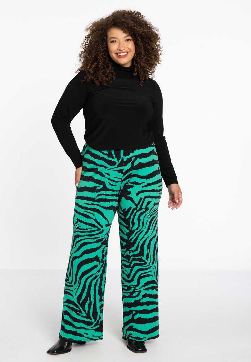 Wijd beenbroek in groen met zwarte zebraprints, gecombineerd met een aansluitend zwart langemouwen shirt, dat de gladde stoftextuur benadrukt.