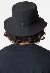 Black bucket hat made of textured fabric with a rounded top and wide brim. Features a small Swedish flag emblem on the back.