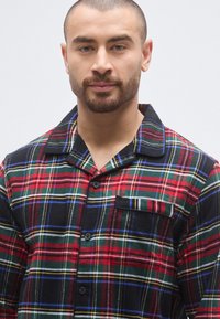 Czerwona i zielona flanelowa koszula nocna w kratę z kołnierzykiem, przednią kieszenią i zapięciem na guziki. Miękka faktura z różnorodnymi wzorami pasków.