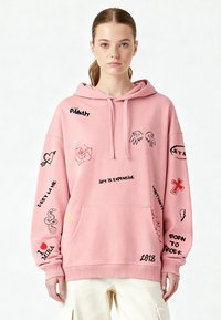 Hoodie rose avec divers designs graphiques noirs et rouges, incluant du texte et des icônes. Comprend une poche frontale et un capuchon avec cordon.