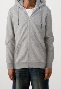 Hoodie zippé gris en tissu doux. Comprend une fermeture éclair à l'avant, deux poches avant et une capuche avec cordon de serrage. Coupe décontractée.