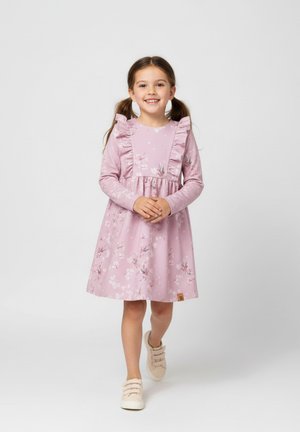 Różowa sukienka w kwiaty z długimi rękawami, z falbankami na ramionach i marszczonym taliowaniem. Noszona z beżowymi butami, z logo na metce przy dolnym brzegu.