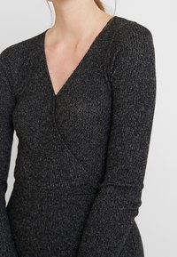 Mörkgrå långärmad topp med V-ringning och omslutande design, med ett texturerat stickat tyg och åtsittande silhuett.