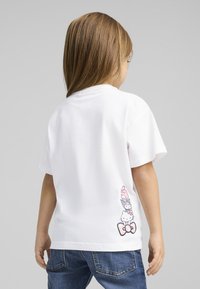 Hvid bomulds t-shirt med tryk af tegneseriefigurer i pastelfarver på den nederste ryg. Korte ærmer og en afslappet pasform.