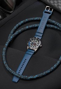 Zegarek Timex z czarną tarczą, niebieskim gumowym paskiem i stalową kopertą; w komplecie z plecionym czarnym i niebieskim sznurkiem.