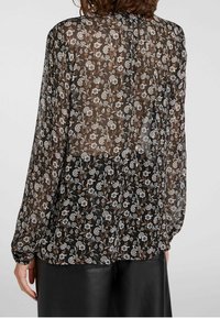 Doorzichtig zwart blouse met bloemmotief in wit en bruin, lange mouwen en knoopsluiting bij de hals. Geweven en lichtgewicht stof.