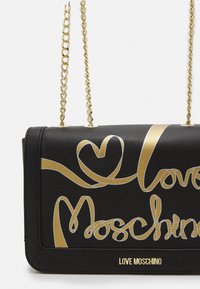 Borsa a mano in pelle nera con logo dorato in corsivo "Love Moschino" e design a forma di cuore, completa di tracolla in catena dorata per il trasporto.