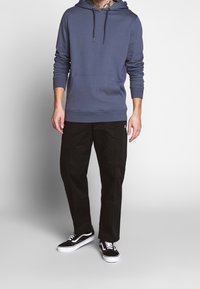 Mörkblå huvtröja med framficka och dragsko i huvan, kombinerad med svarta byxor och svarta sneakers med vita sulor.