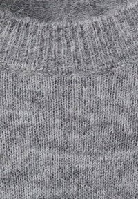 Siv sweater iz pletenine z rebrasto teksturo in mekim, puhastim zaključkom. Enakomerna šivnost z svetlimi barvnimi odtenki po celotni površini.