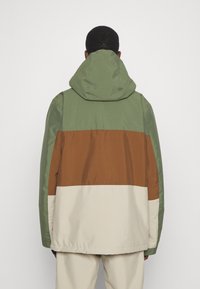 Chaqueta con capucha que presenta un diseño a bloques de color con paneles verdes, marrones y crema. Fabricada en un tejido suave y duradero con un corte relajado.